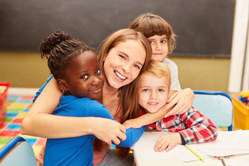 Adult hugging three smiling children, one of whom is Black